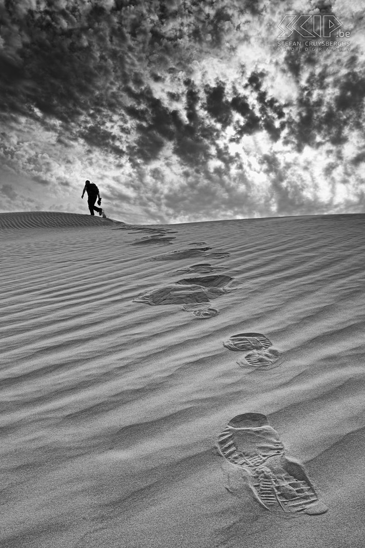 Wandelen in de duinen Ik had een idee om een foto te maken met de voetsporen van een van mijn vrienden die een zandduin op wandelt. Gelukkig waren er de tweede dag prachtige wolkenformaties. Het was een van die weinig momenten waar alles perfect samenkwam en in zwartwit levert dit dan ook een heel sterk beeld op. Stefan Cruysberghs